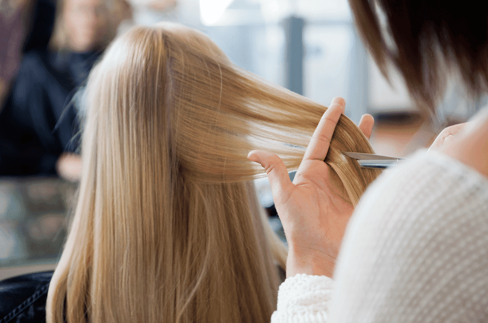 Hairdresser trimming a client's long blonde hair.